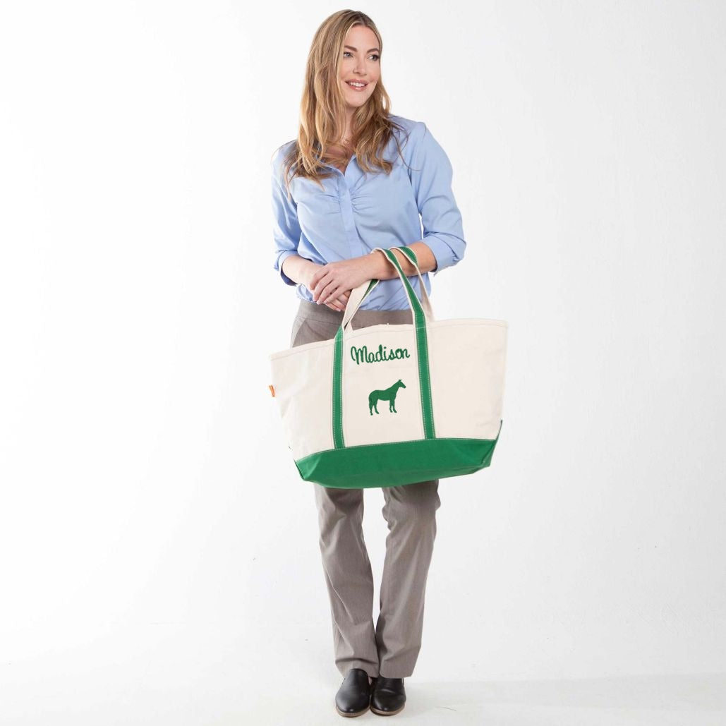 Woman holding a green tote bag with and a horse icon with a name embroidered above it.