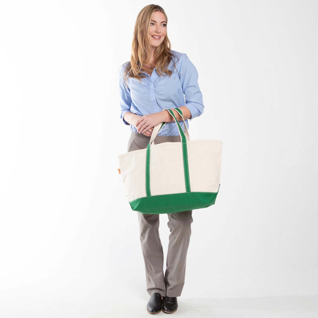 Woman holding a white tote bag with green trim on a white background